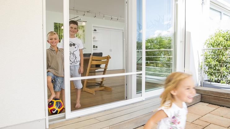 Spielende Kinder vor Insektenschutztür zum Schieben auf Terrasse
