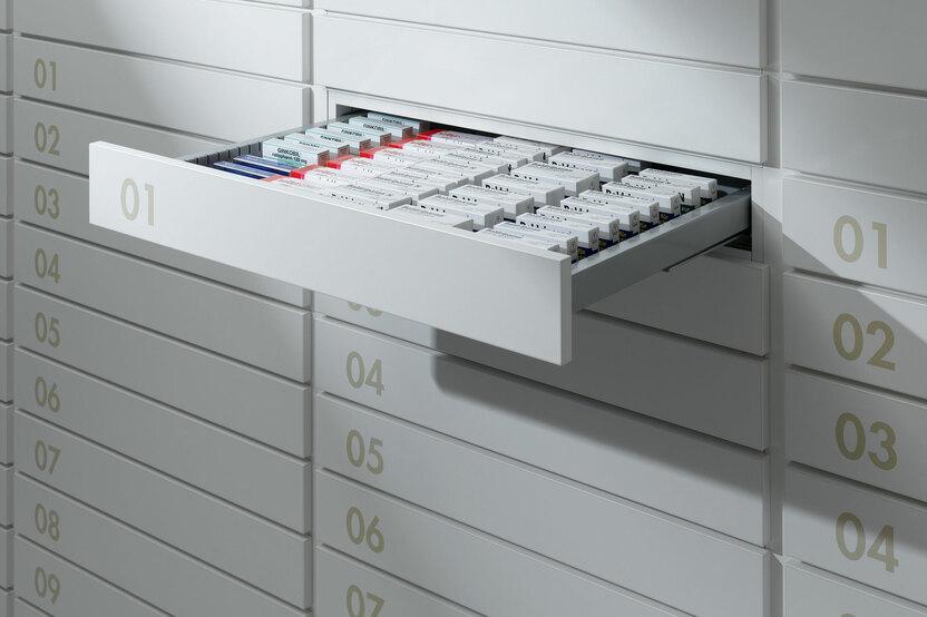 Detailaufnahme von schmalen weißen Medikamentenschubläden mit dezenter Nummerierung und sichtbarer Medikamentenaufteilungen.