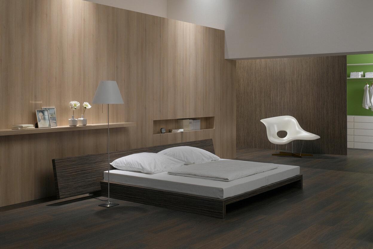 Schlafzimmerimpression mit Holzverkleidung an Wand Schlafzimmerimpression von Bett, Nachtisch und Sideboard mit Holzverkleidung an Wand und indirektert Beleuchtung